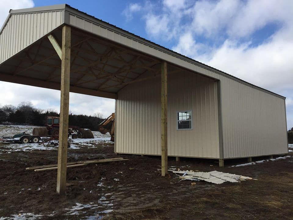 Tan metal agricultural building with a covered awning, blue sky.