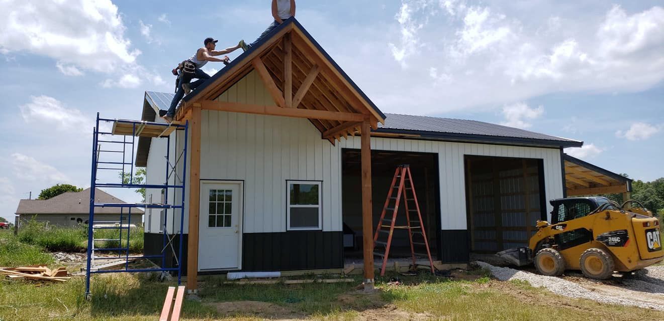 Construction of a white building with black lower siding and a yellow skid steer. A worker is on the roof.