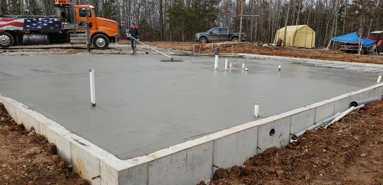 Freshly poured concrete foundation with plumbing pipes, construction site.