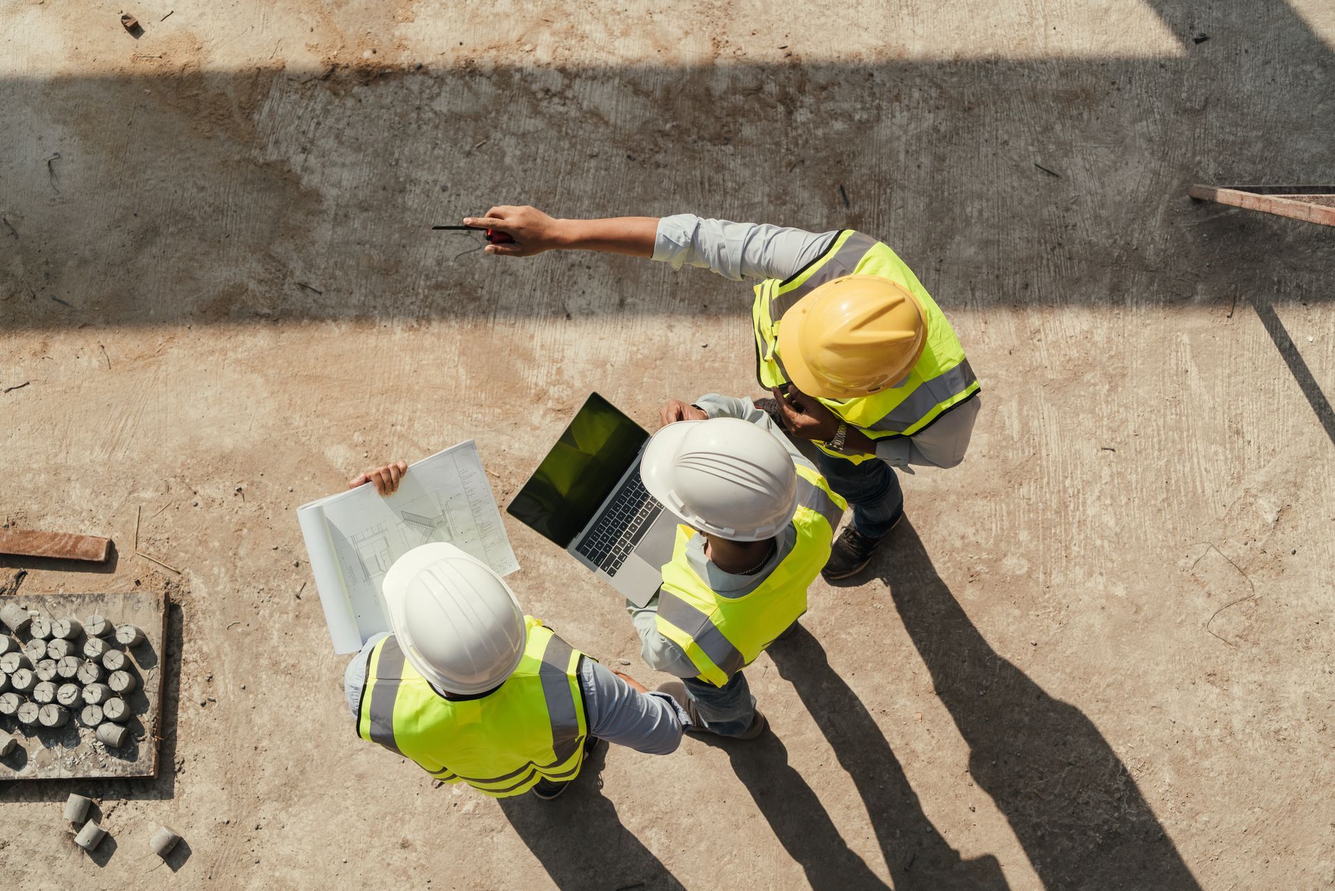 Overhead view of three construction workers wearing safety helmets, reviewing plans.