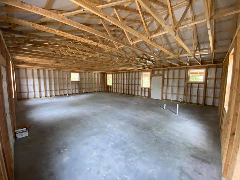 Interior view of a new, unfinished building, with wooden frame, concrete floor, and windows.