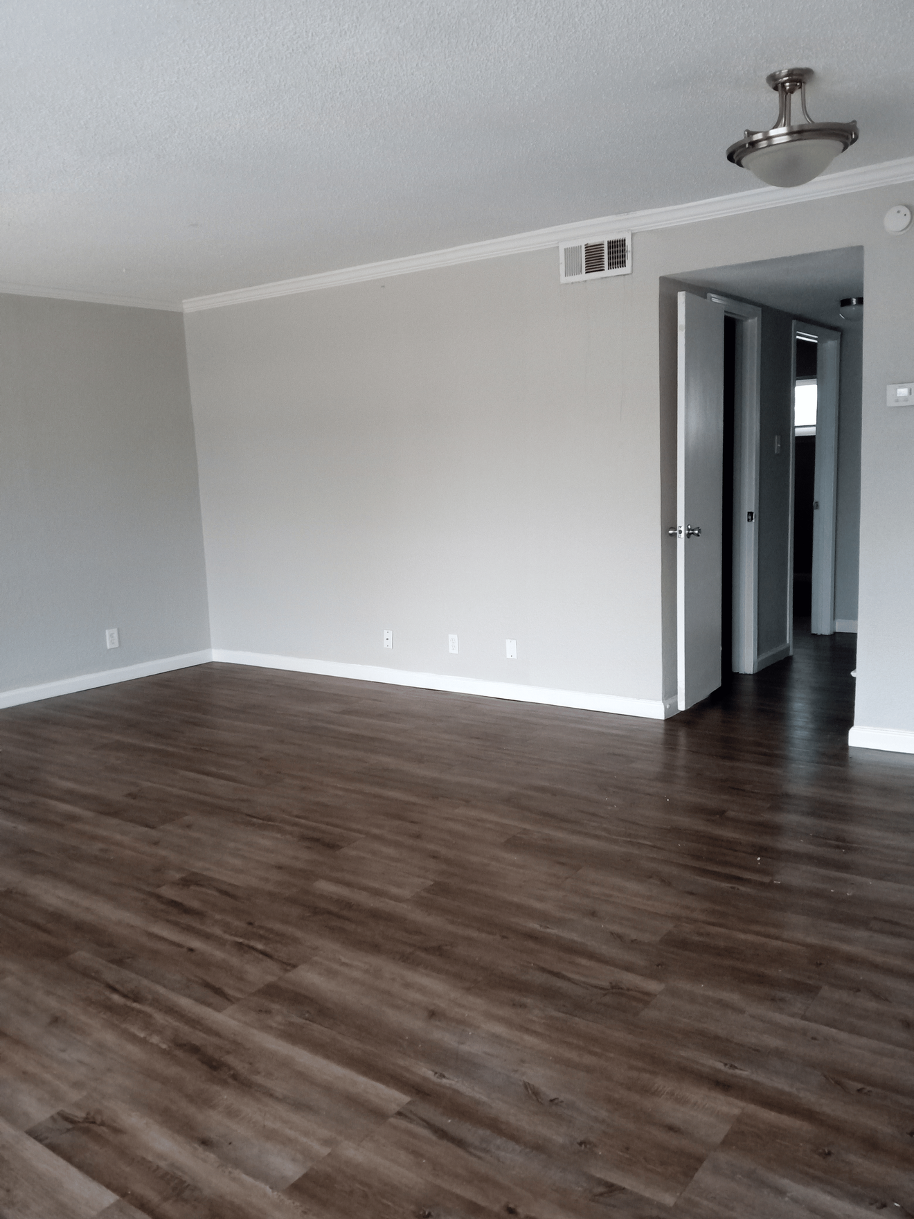 Empty room with gray walls, dark wood-look flooring, white trim, and an open doorway.