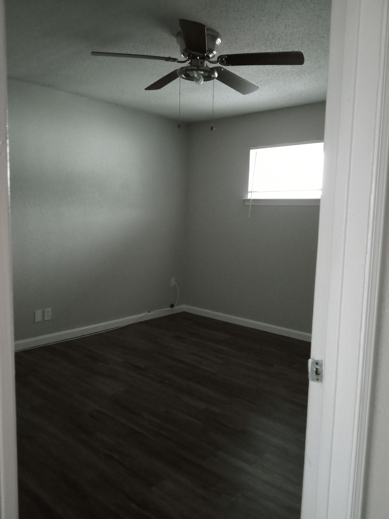 Empty room with dark wood floor, gray walls, ceiling fan, and small window.