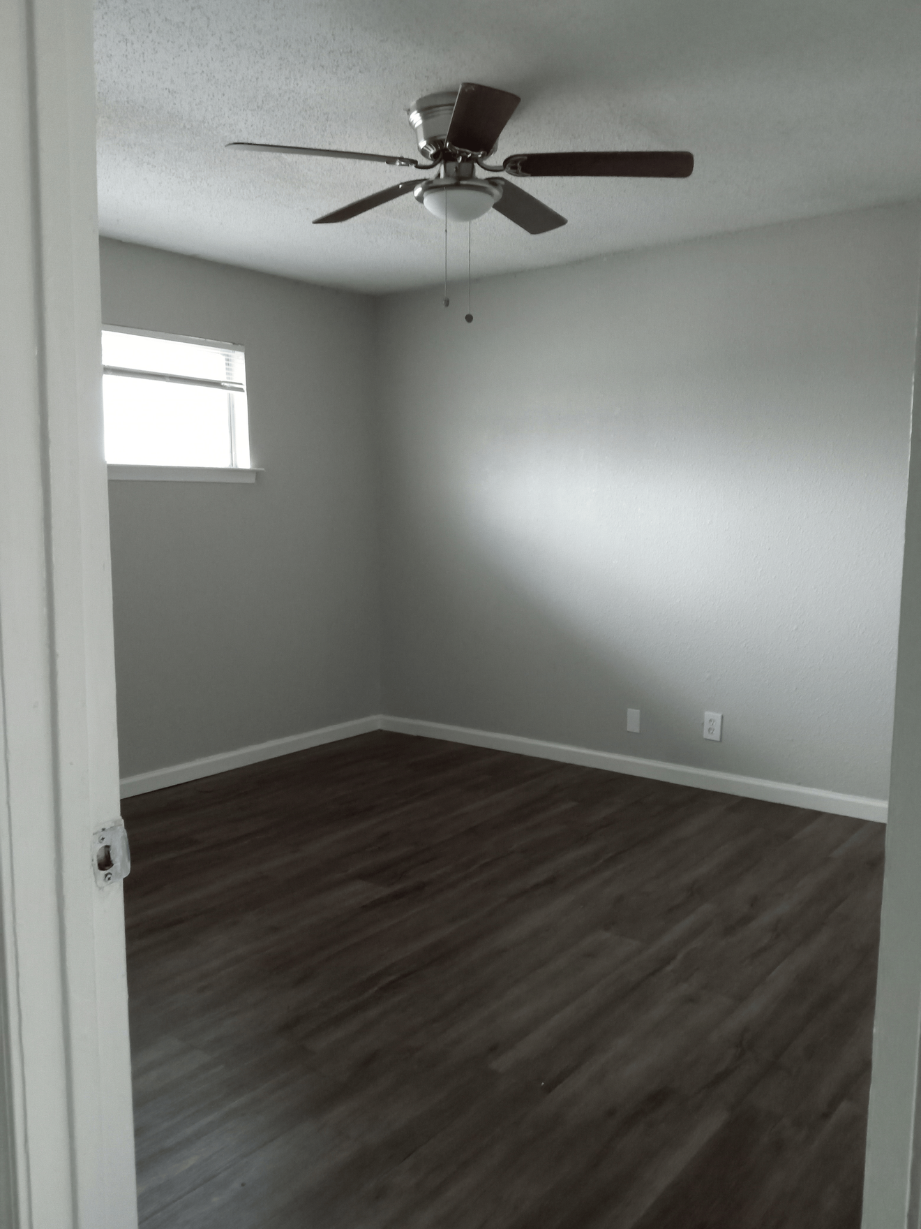 Empty bedroom with gray walls, dark wood-look floor, window, ceiling fan.