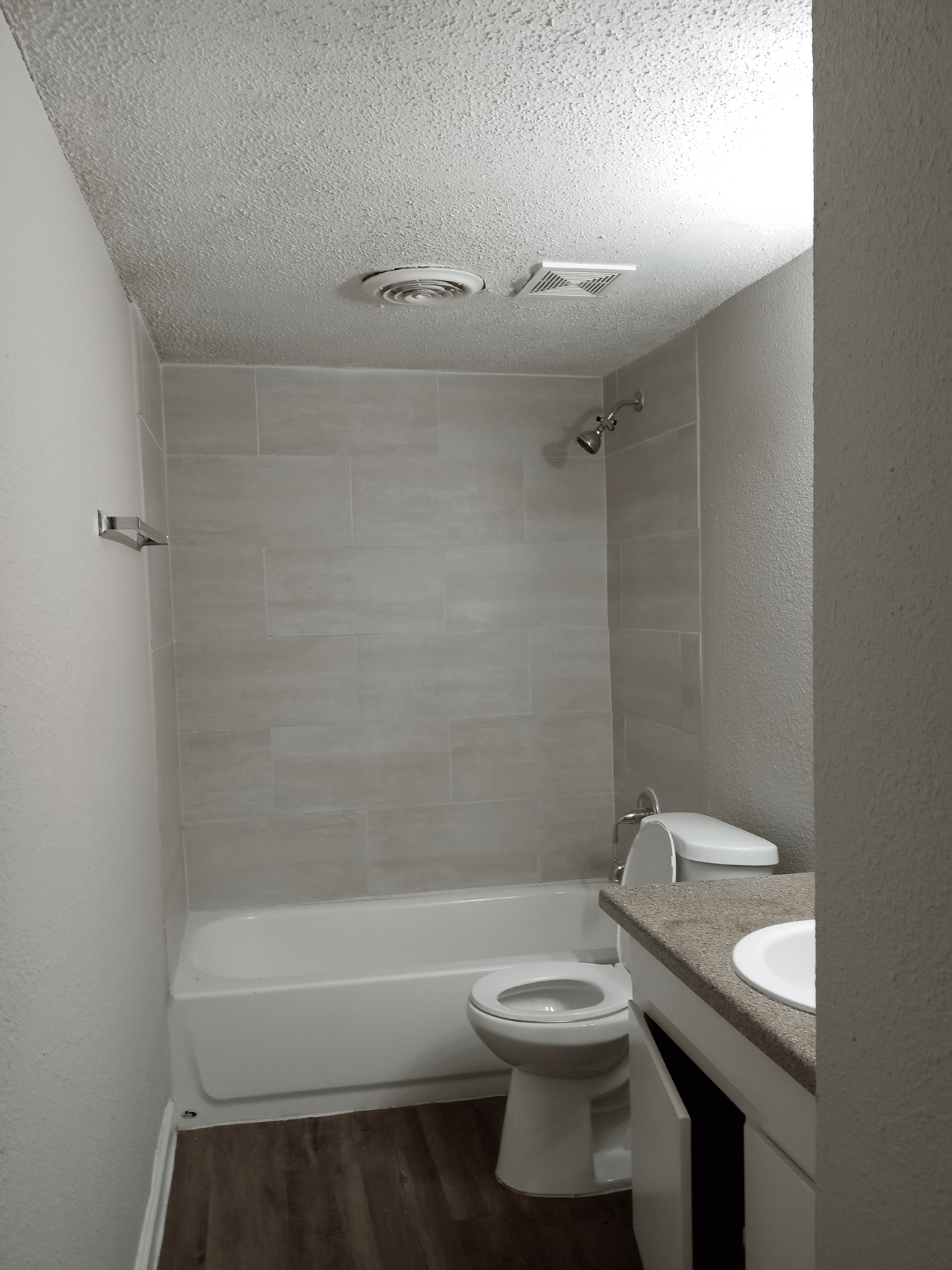Bathroom with a white tub, gray tiled shower walls, and a toilet.