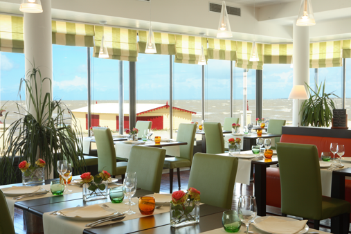 Un restaurant avec des tables et des chaises et une vue sur l'océan réalisé par mes services d'architecte d'intérieur