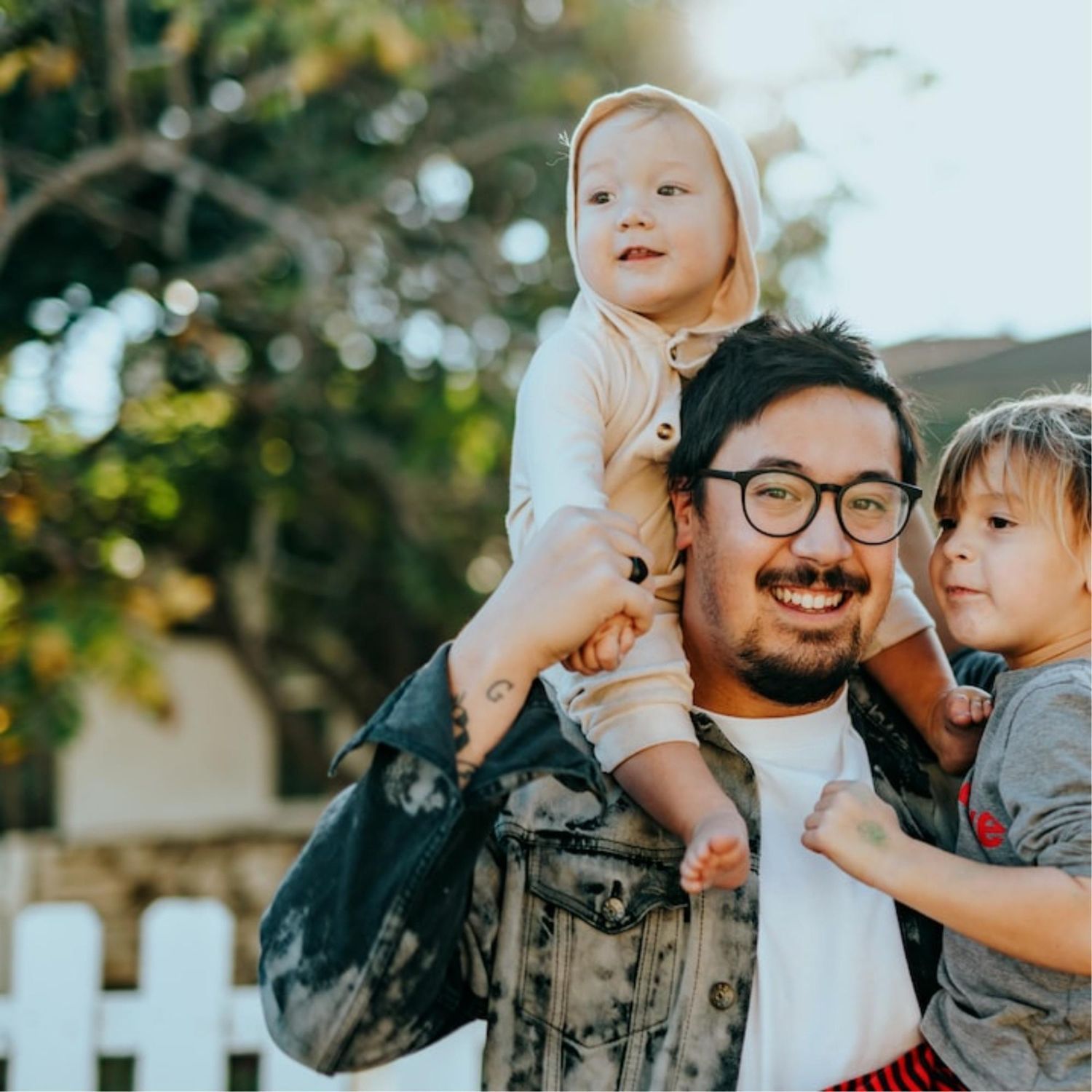 Family sitting on the floor smiling at a toddler. Mom holding child. Dad holding child's hand. Living room setting.