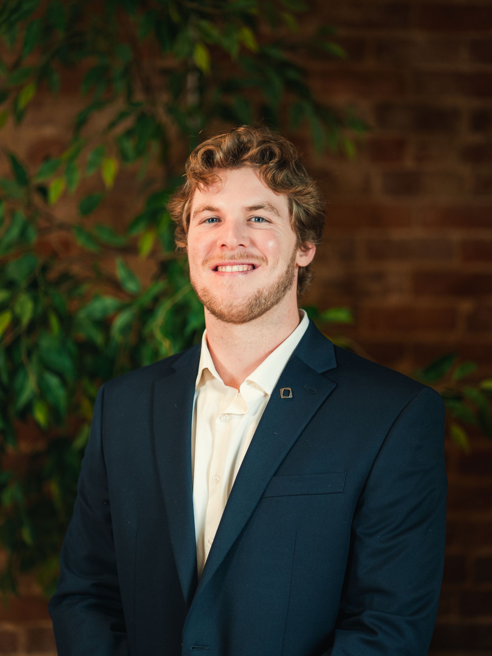 Woman with brown hair, smiling, wearing an orange top and necklace, set outdoors.
