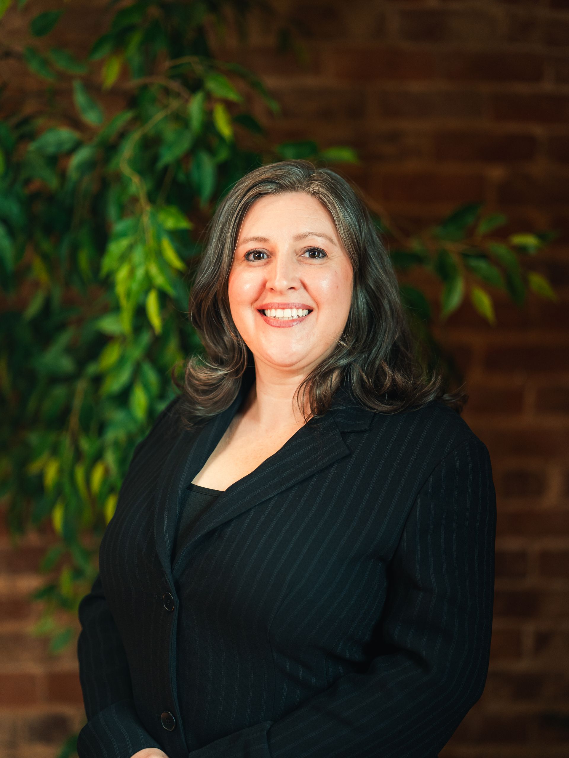 Woman with brown hair, smiling, wearing an orange top and necklace, set outdoors.