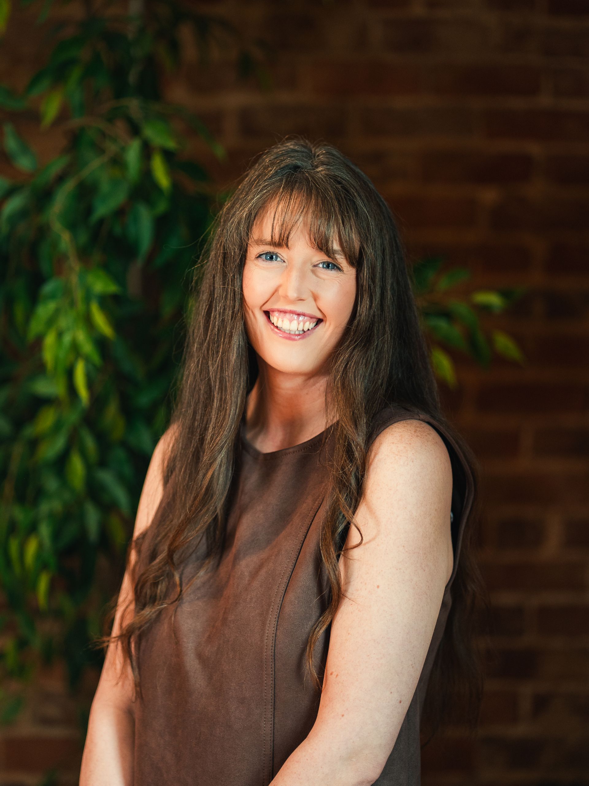 Bald man in glasses smiles, leans against a white wall wearing a blue suit and white shirt.