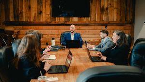 Man and woman reviewing paperwork at a table, both holding pens, with a laptop and coffee cups nearby.