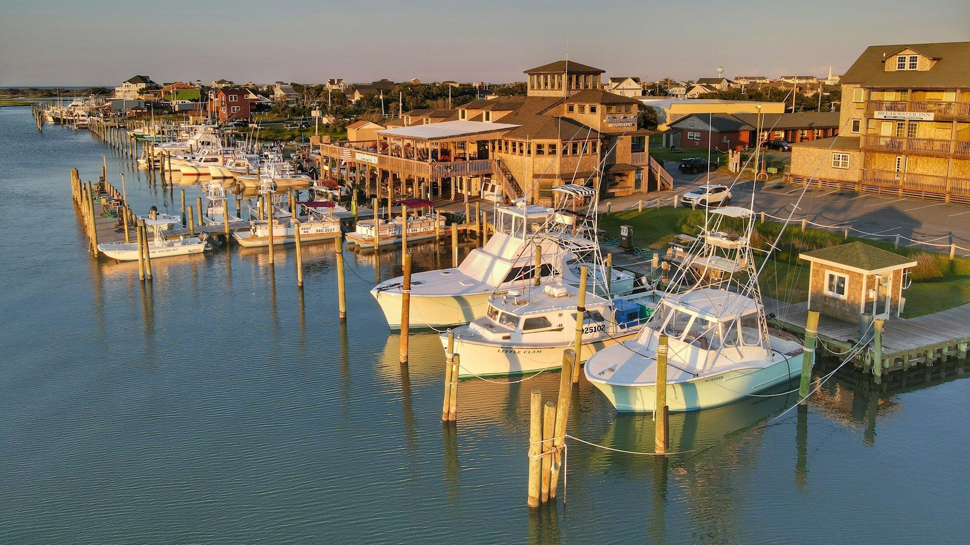 Boats docked at a coastal marina, with a multi-story restaurant and buildings in the background.