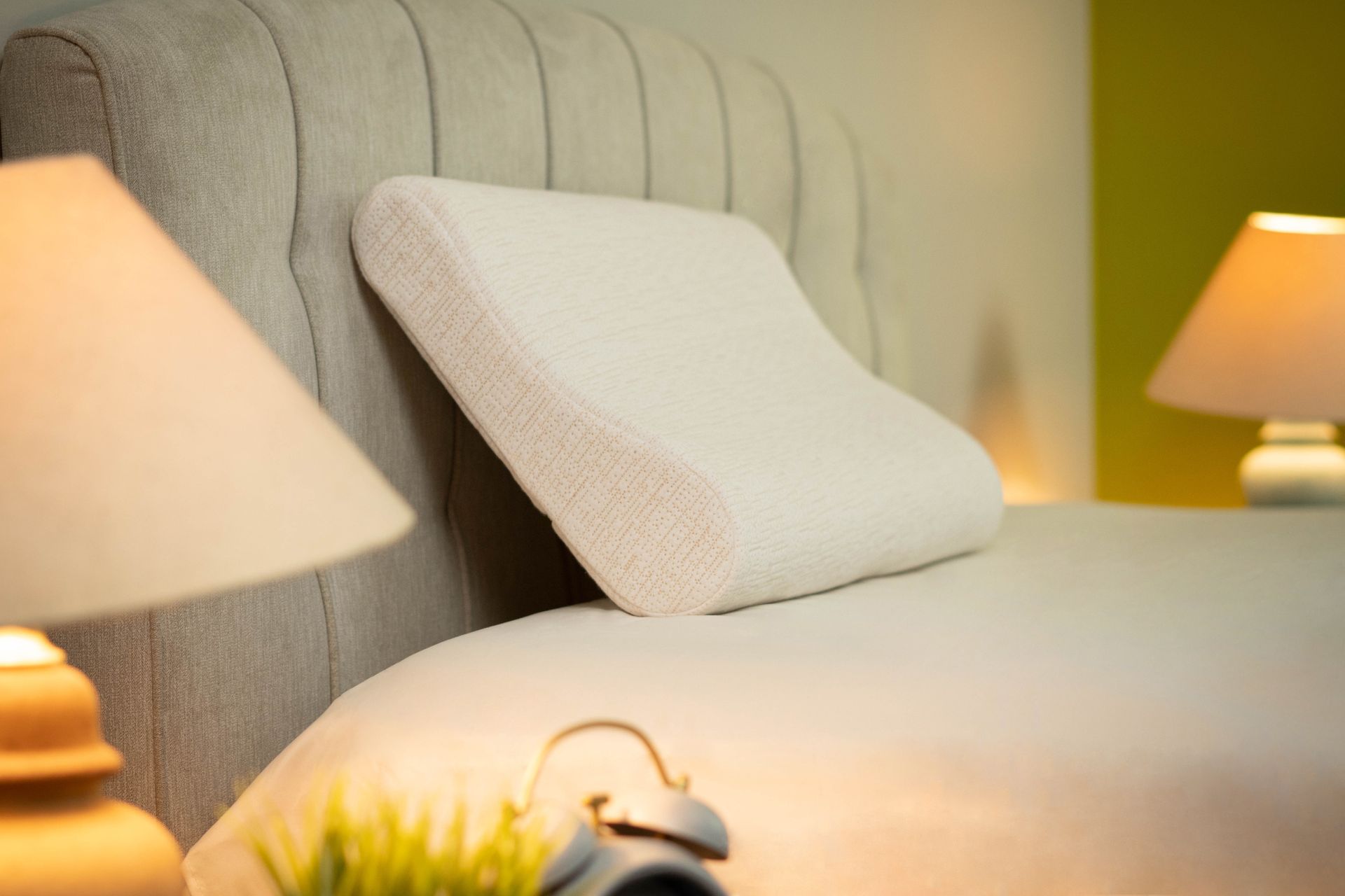 Una almohada blanca está encima de una cama junto a una lámpara.