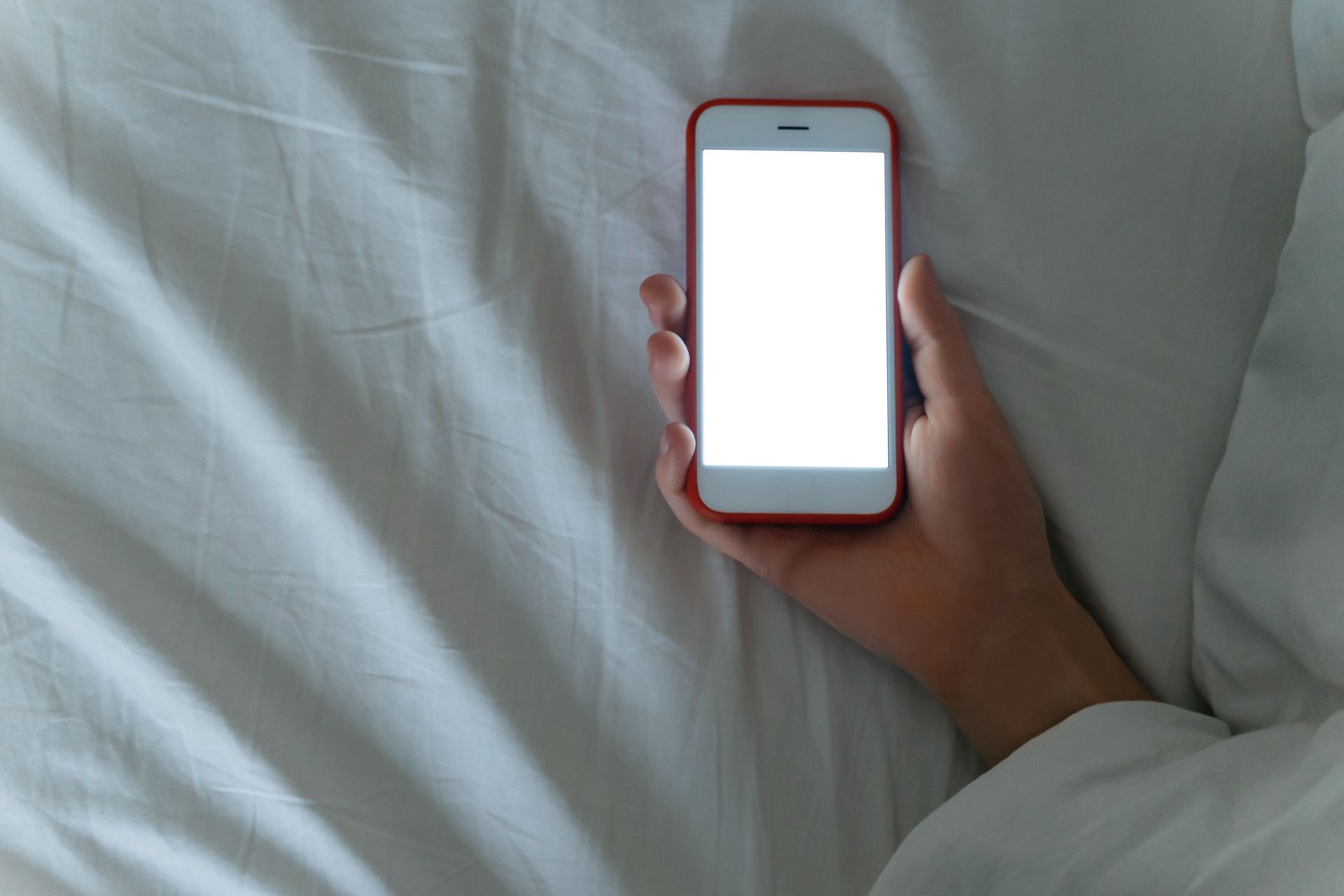 Una persona está acostada en la cama sosteniendo un teléfono celular con una pantalla blanca.