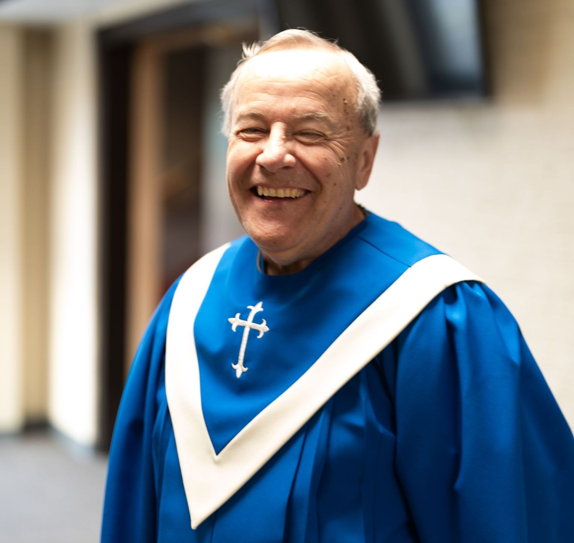 Man in blue clerical robe with white collar, smiling at the camera.