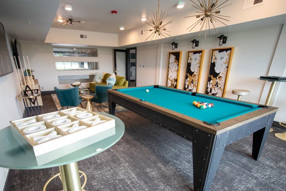 Pool table in a lounge area, teal felt, black frame. Three art pieces, starburst lights, round table with pastries.