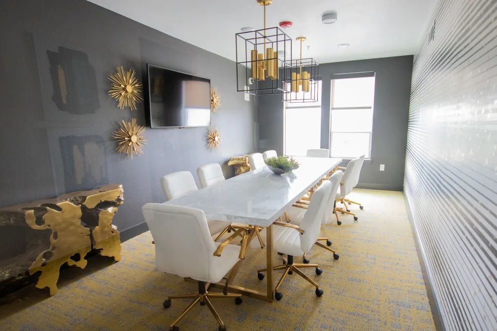 Conference room with white chairs, gold accents, marble table, and geometric wallpaper.