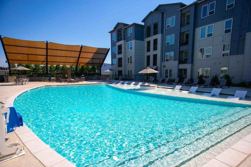 Pool with lounge chairs and apartment building in the background on a sunny day.