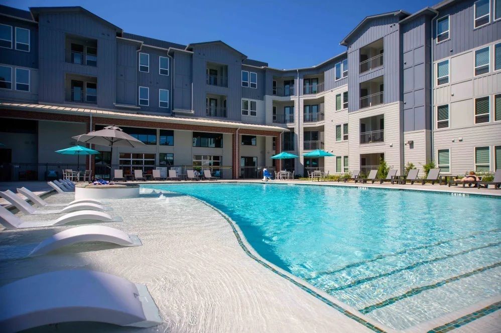 Swimming pool in front of a multi-story apartment building on a sunny day.