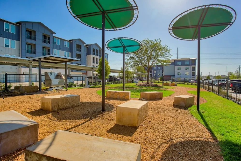 Outdoor park with stone seating, green sunshades, and multi-story apartment buildings.