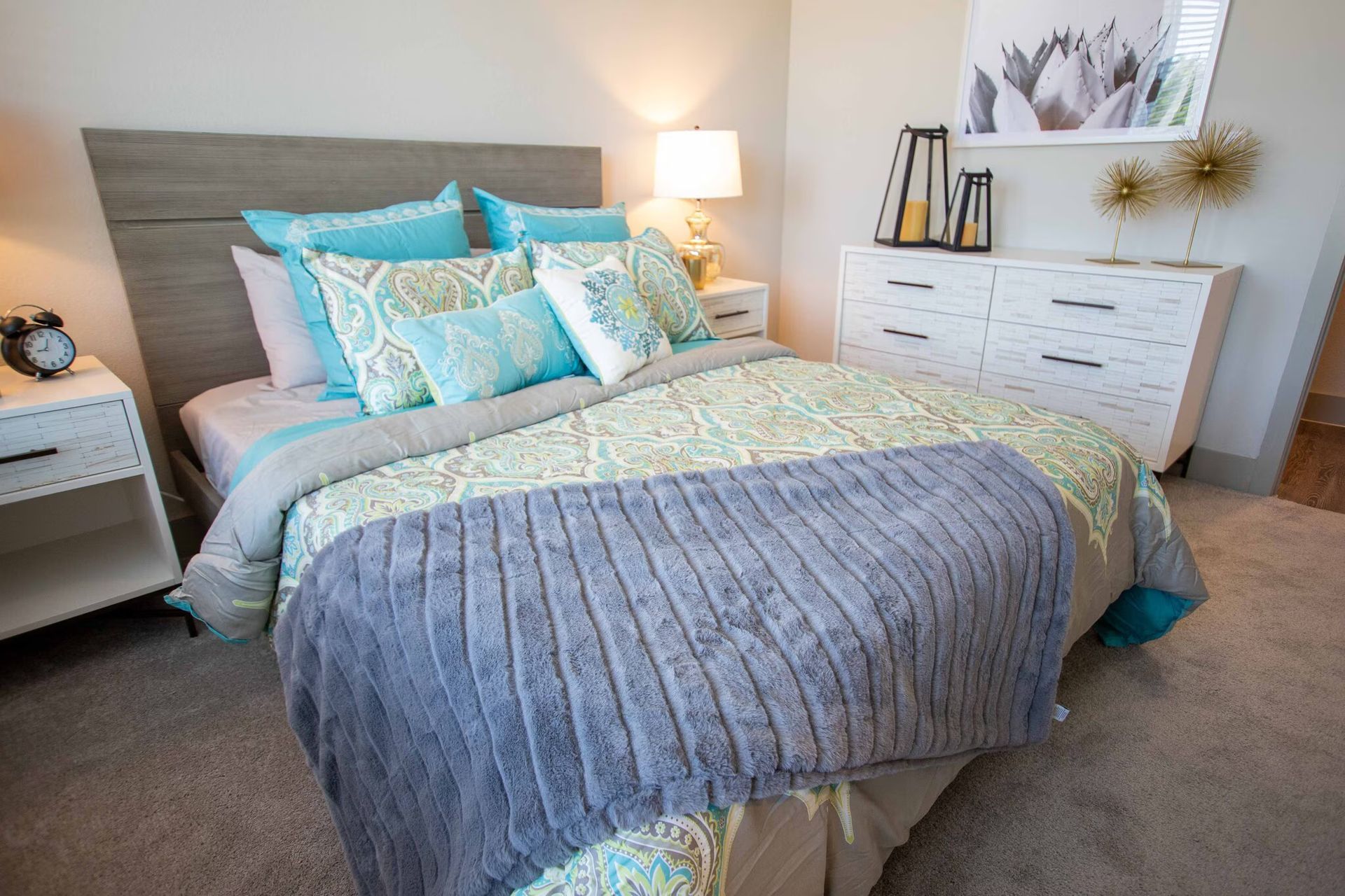 Bedroom with light gray headboard, aqua bedding, white dresser, and nightstands.