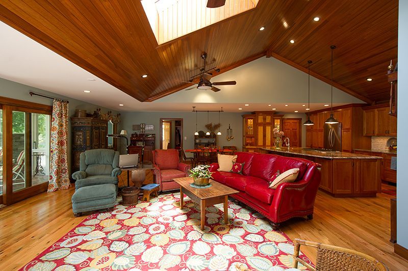 Open-concept living area with wood ceiling, red leather sofa, patterned rug, and kitchen in background.