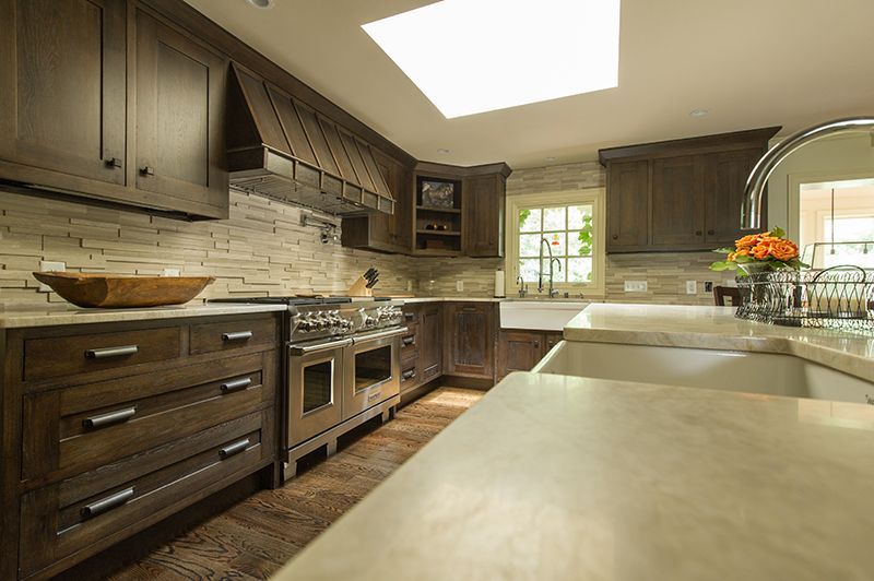Dark wood kitchen with stone backsplash, stainless steel stove, and a light-colored countertop.
