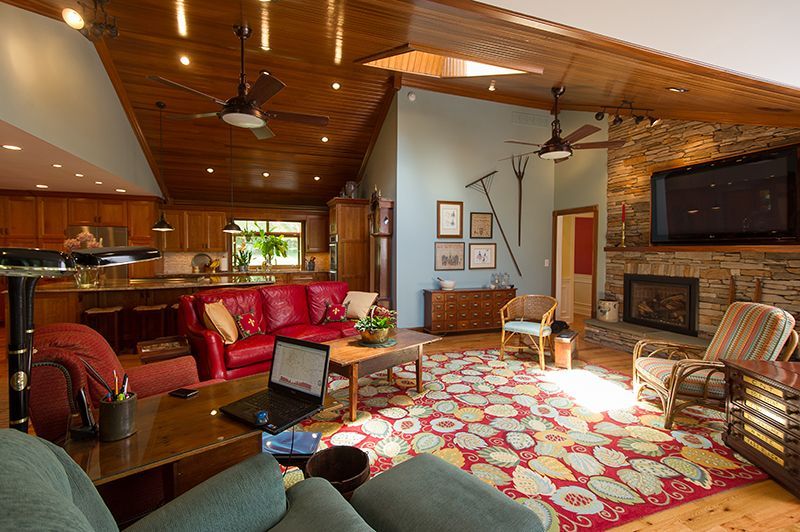 Cozy living room with red couch, fireplace, and colorful rug; wooden ceiling, laptop on table.