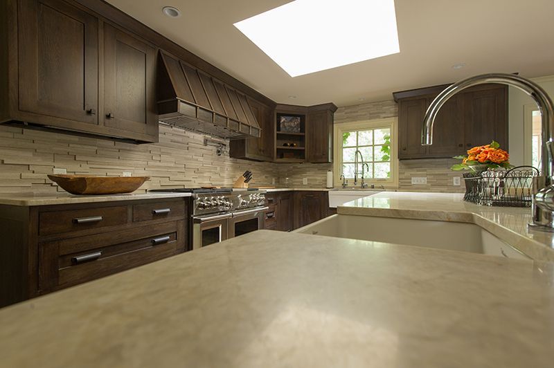 Dark wood kitchen with stone backsplash, skylight, and stainless steel appliances.