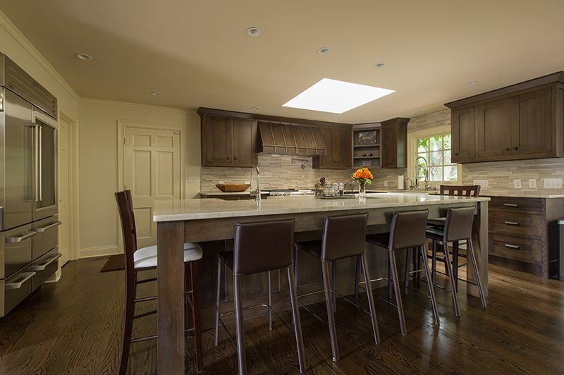 Spacious kitchen with a large island, brown cabinets, stainless steel fridge, and skylight.