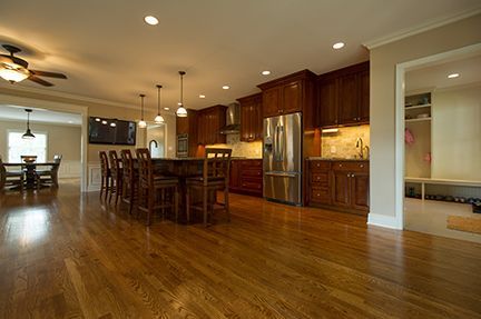 Spacious kitchen with island seating, dark wood cabinets, and stainless steel refrigerator; dining area and hallway visible.