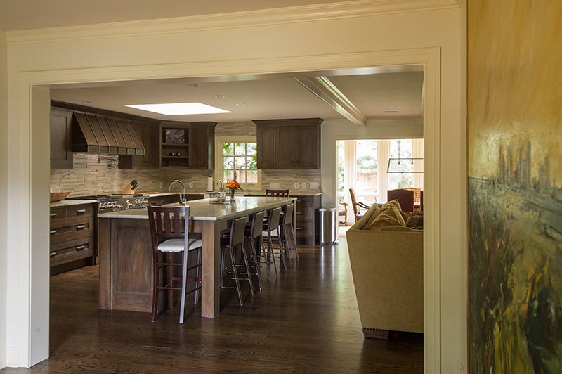 Kitchen interior with dark wood cabinets, island with stools, and an adjoining living area.