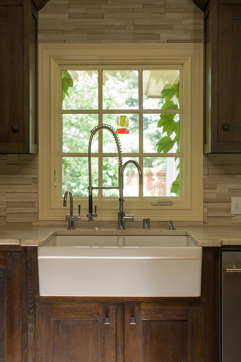 Kitchen sink in front of a window with greenery, dark cabinets and neutral tile backsplash.