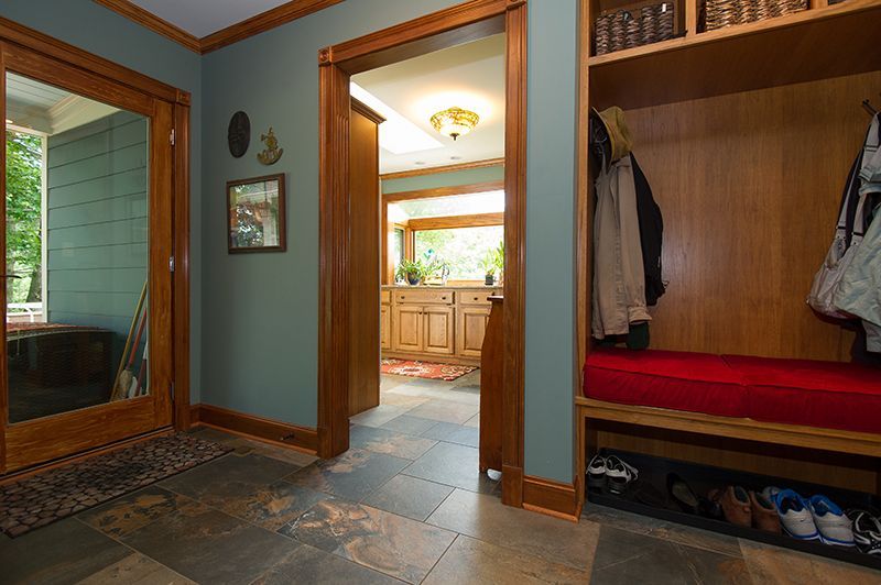Hallway with teal walls, wooden trim, slate floor, and a mudroom with coats and shoes.