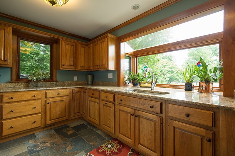 Kitchen with light wood cabinets, granite countertops, and a large window overlooking trees.
