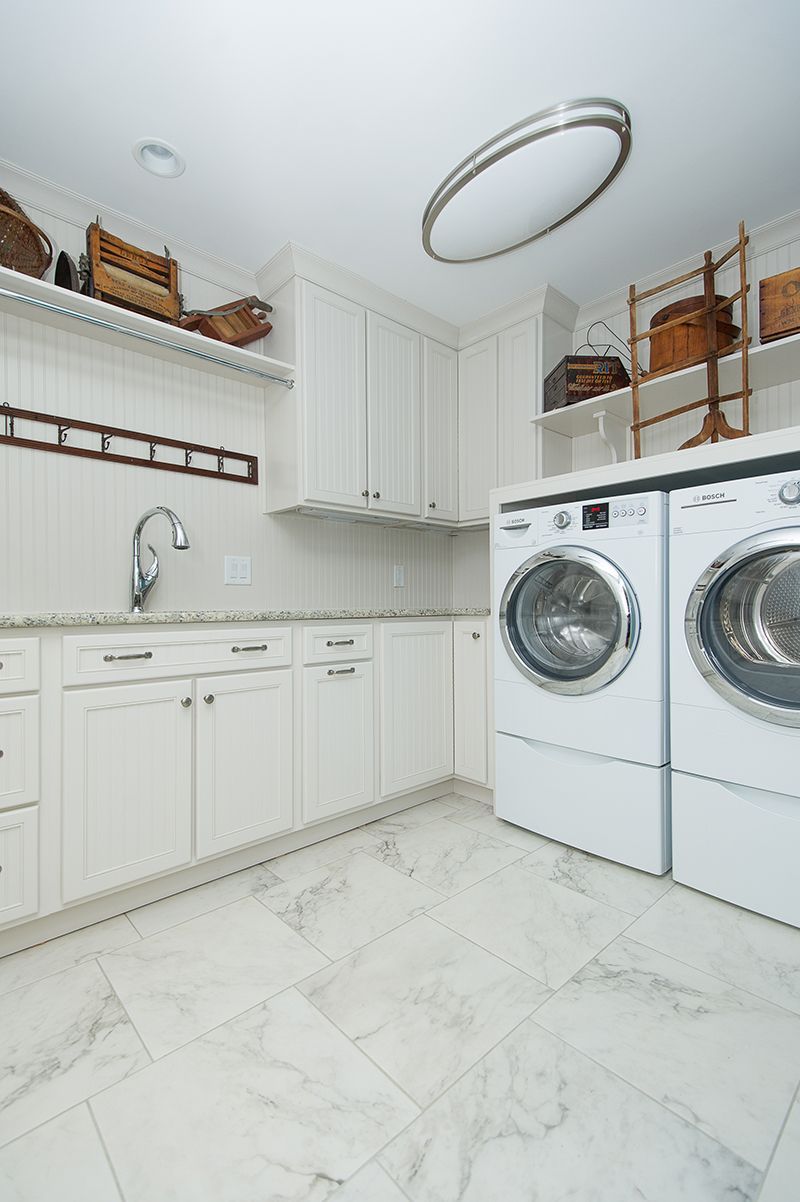 Bright white laundry room with washer, dryer, cabinets, and open shelving, decorated with wicker baskets.