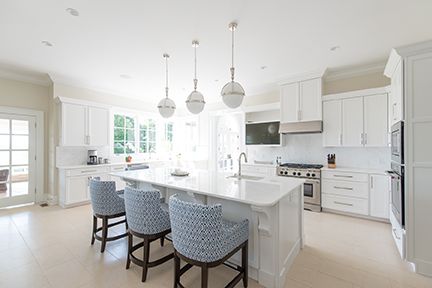Bright white kitchen with island, three blue patterned bar stools, and pendant lights.