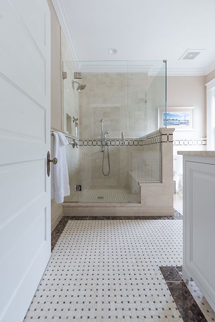 Bathroom with glass shower, white and black tile floor, light beige walls, and white door.