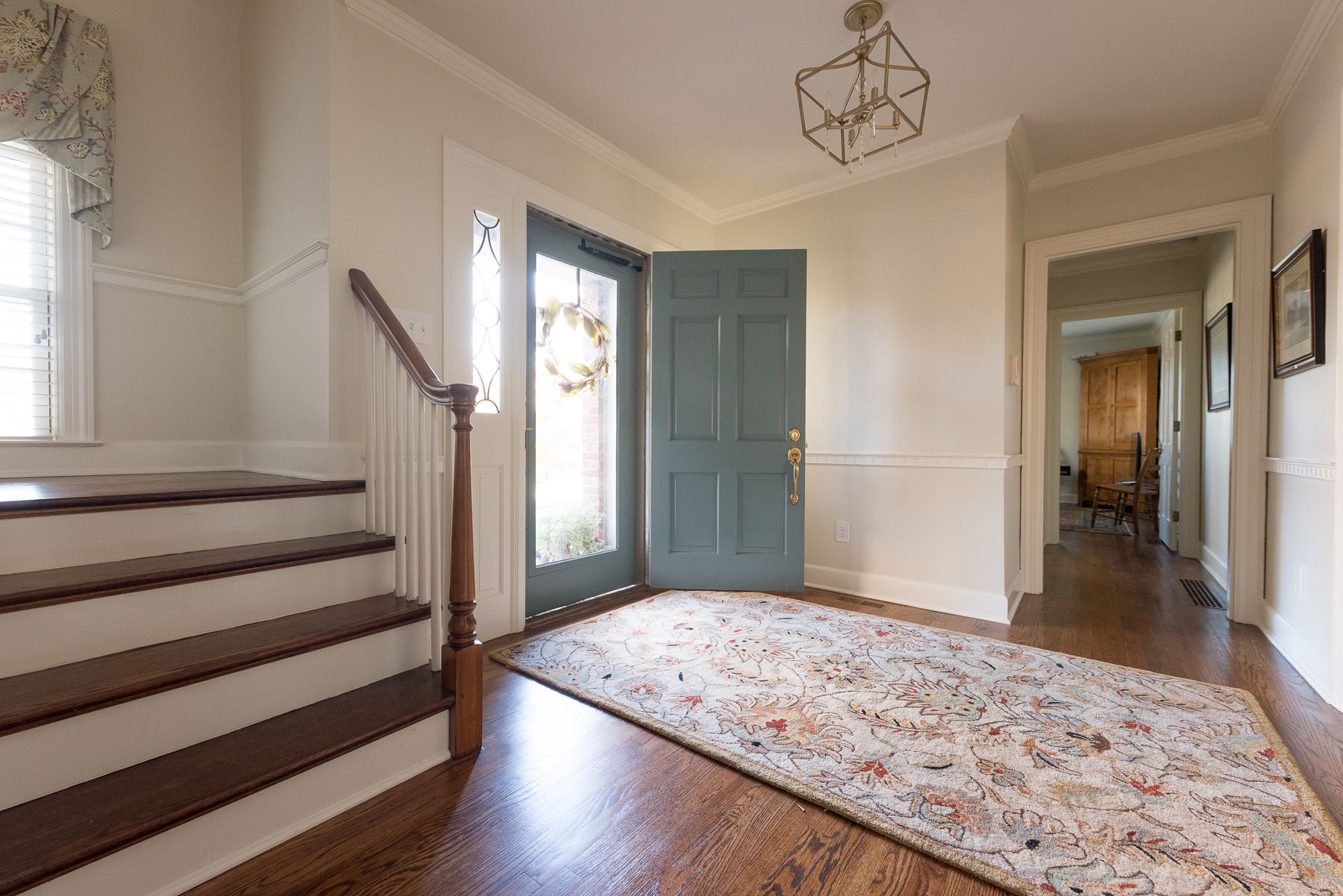 Entryway with teal door, hardwood floors, staircase, and floral rug.