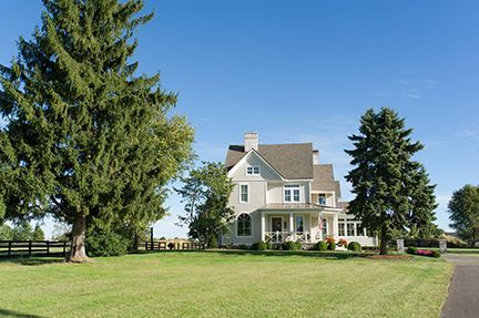 Two-story white house with green lawn and trees under a clear blue sky.