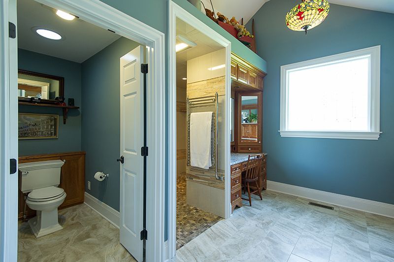 Bathroom with blue walls, featuring a toilet, shower, vanity, and a stained-glass chandelier.