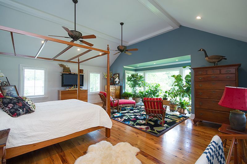 Bedroom with canopy bed, wooden floor, blue wall, and a sunroom filled with plants.