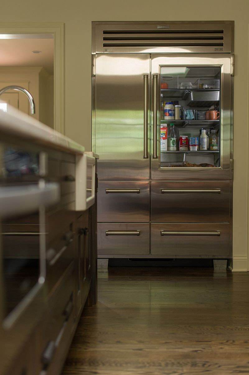 Stainless steel refrigerator with the door open, revealing shelves of food. Dark wooden floor.