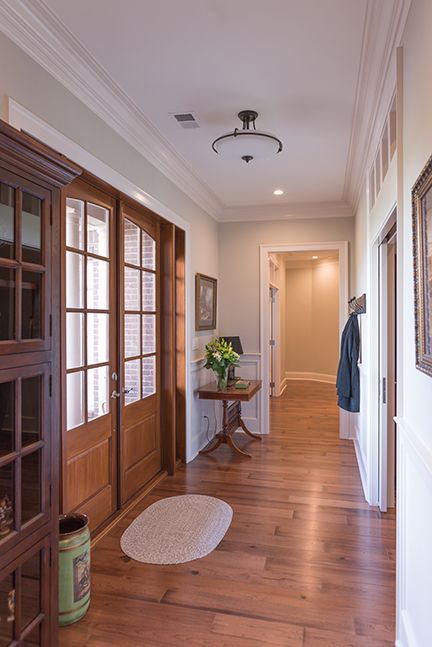 Hallway with hardwood floors, wood-framed doors, side table with flowers, and a rug.