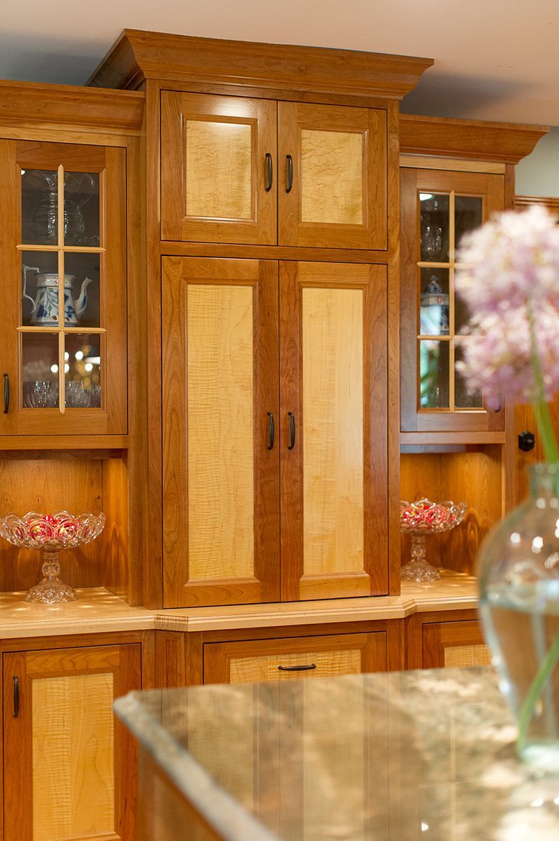 Wooden kitchen cabinets with glass-paneled doors and granite countertops, with a flower in the foreground.