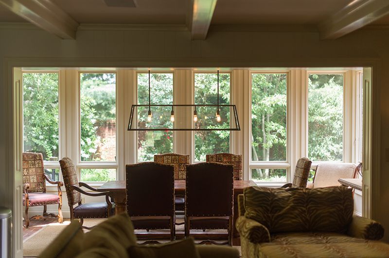 Dining room with table, chairs, and large windows overlooking a wooded area.