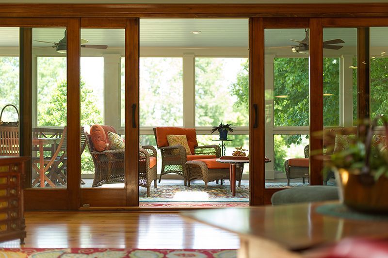 Open wooden sliding doors reveal a sunroom with wicker furniture, greenery, and natural light.