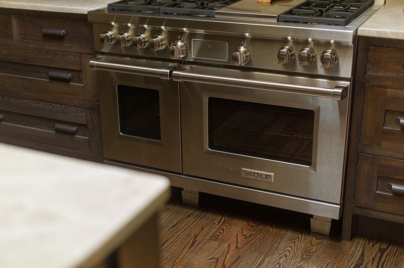 Stainless steel oven in a wooden kitchen, featuring two ovens and a stovetop.