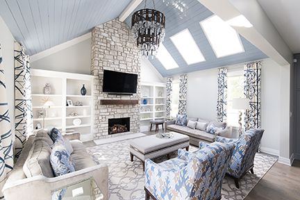 Living room with stone fireplace, blue ceiling, light furniture, and patterned curtains.