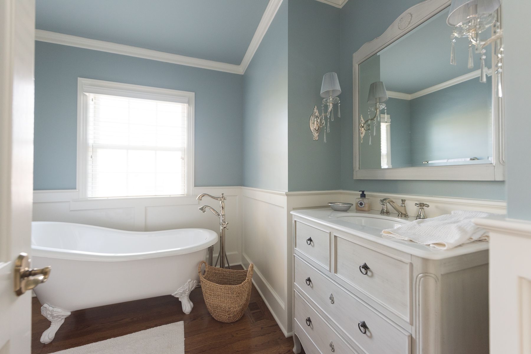 Bathroom with clawfoot tub, white vanity, pale blue walls, and a large mirror.